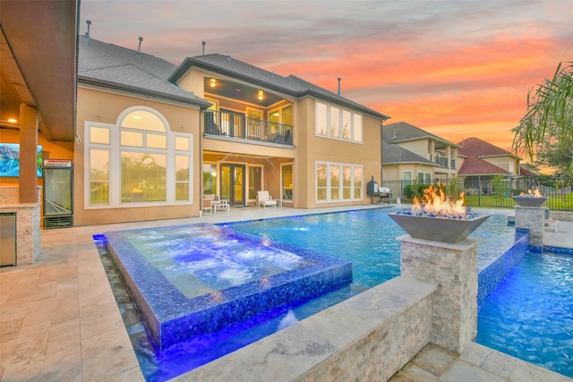 pool at dusk with grilling area, pool water feature, an in ground hot tub, a patio area, and an outdoor fire pit