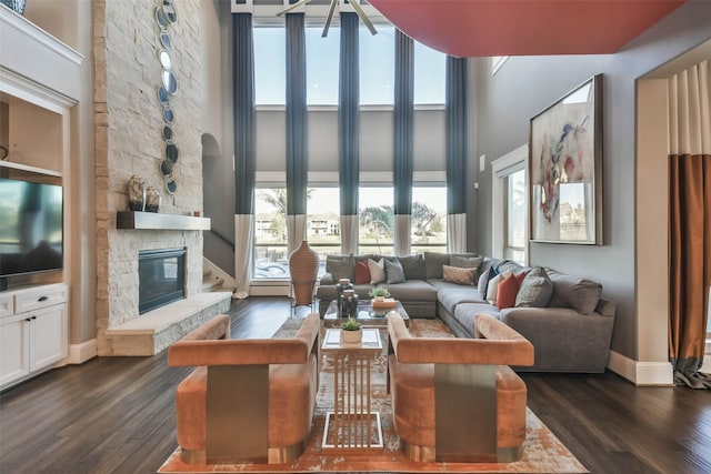 living room with a stone fireplace, a towering ceiling, and dark hardwood / wood-style floors