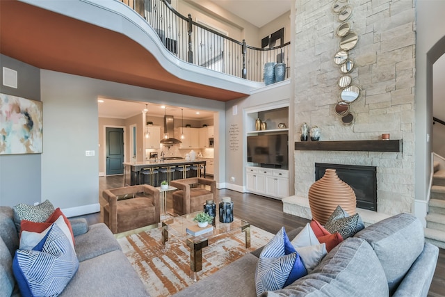 living room with a stone fireplace, dark hardwood / wood-style flooring, a towering ceiling, and ornamental molding