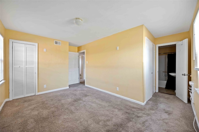 unfurnished bedroom with ensuite bathroom, light carpet, and a closet