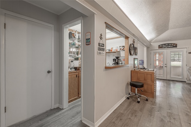 hallway featuring french doors, a textured ceiling, light hardwood / wood-style flooring, and vaulted ceiling