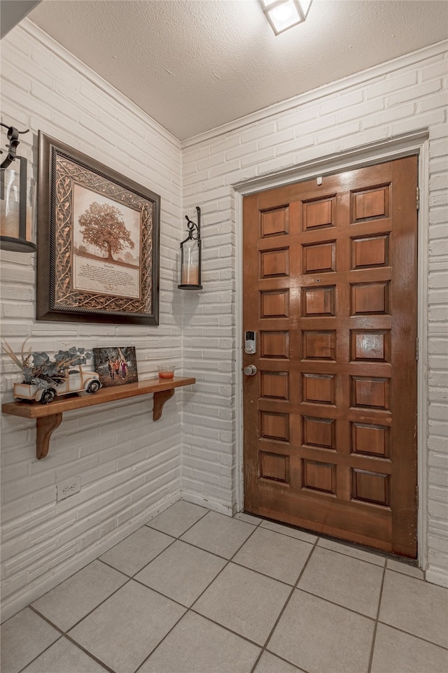 entryway with light tile patterned floors, brick wall, and a textured ceiling