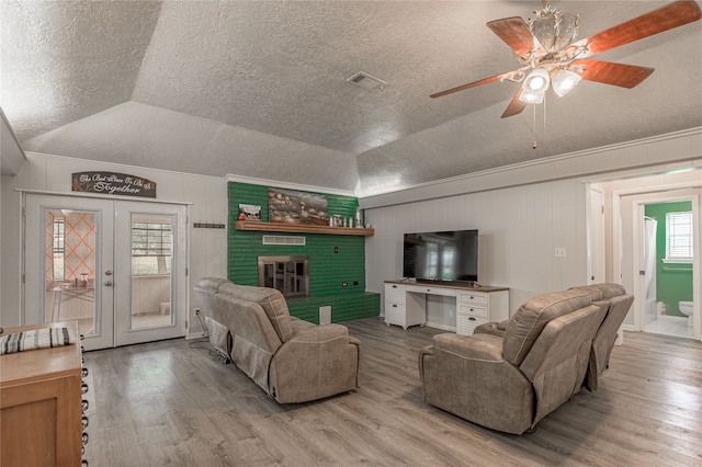 living room with french doors, a brick fireplace, ceiling fan, light hardwood / wood-style flooring, and lofted ceiling