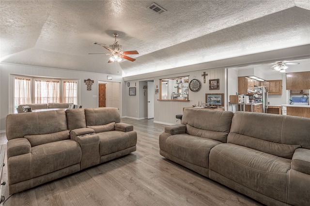 living room featuring a textured ceiling, ceiling fan, vaulted ceiling, and light wood-type flooring