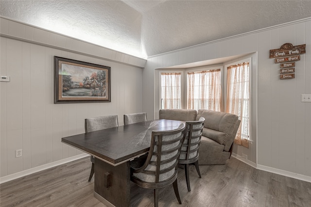 dining space featuring wooden walls, dark wood-type flooring, and a textured ceiling