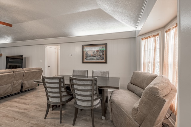 dining area with lofted ceiling, wood walls, light wood-type flooring, and a textured ceiling