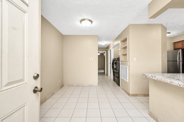 kitchen with light stone countertops, a textured ceiling, stainless steel refrigerator, and light tile patterned flooring