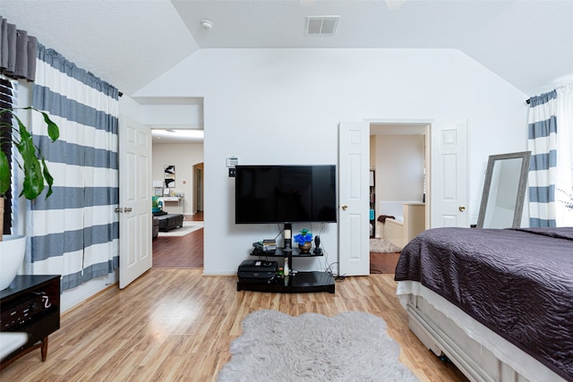 bedroom featuring ensuite bath, vaulted ceiling, and light wood-type flooring