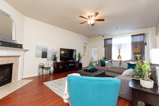 living room featuring a tiled fireplace, ceiling fan, dark hardwood / wood-style flooring, and a textured ceiling