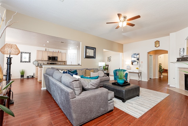 living room featuring a textured ceiling, dark hardwood / wood-style floors, ceiling fan, and a tiled fireplace