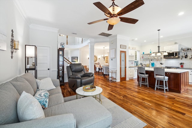 living room with ceiling fan with notable chandelier, light wood-type flooring, and crown molding