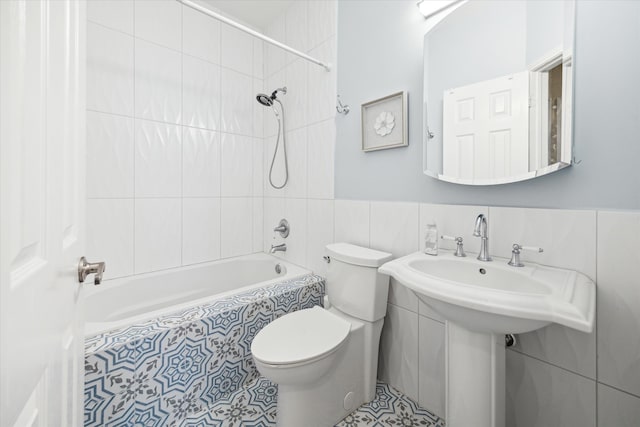 bathroom with tile patterned floors, toilet, tiled shower / bath, and tile walls