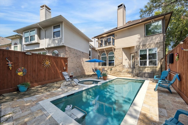 rear view of property with a swimming pool with hot tub, a balcony, and a patio