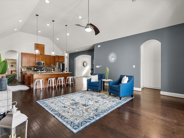 living room with ceiling fan, high vaulted ceiling, and dark wood-type flooring