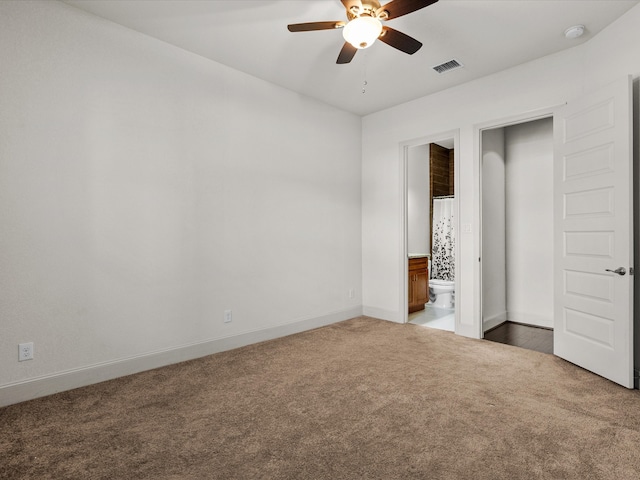 unfurnished bedroom with ceiling fan, ensuite bathroom, and dark carpet