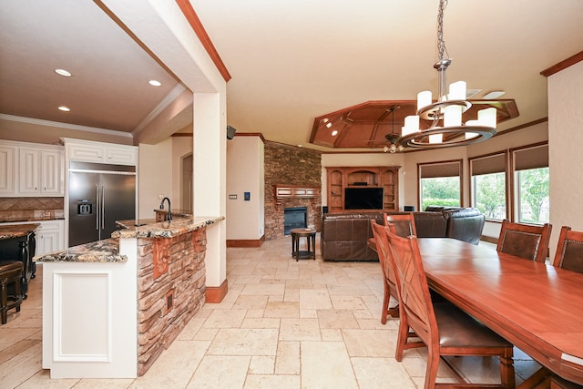 dining space featuring ornamental molding, an inviting chandelier, a stone fireplace, and sink