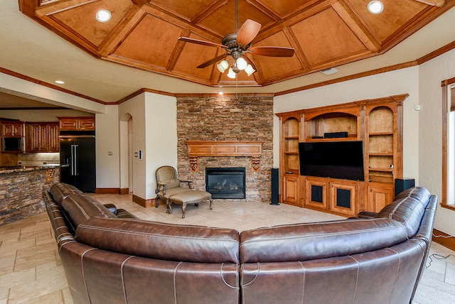 living room featuring coffered ceiling, a stone fireplace, crown molding, ceiling fan, and built in shelves