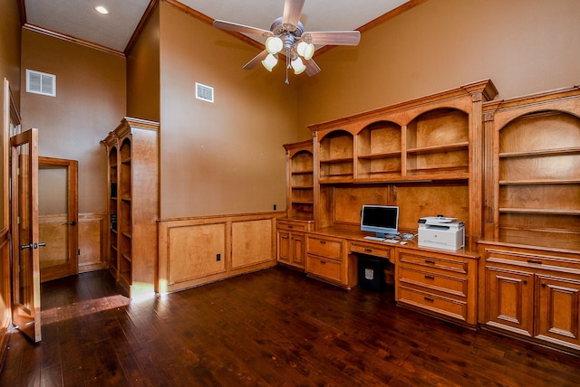 office space featuring ceiling fan, dark wood-type flooring, crown molding, a towering ceiling, and built in desk