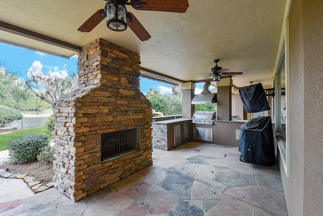 view of patio with ceiling fan, area for grilling, an outdoor stone fireplace, and grilling area