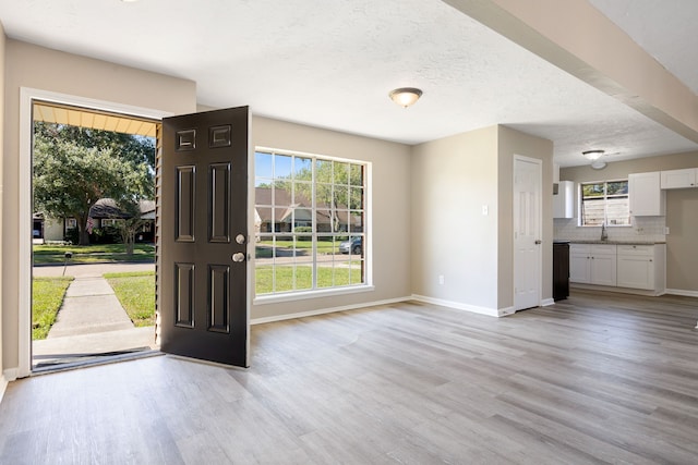 doorway to outside with a textured ceiling, light hardwood / wood-style floors, and sink