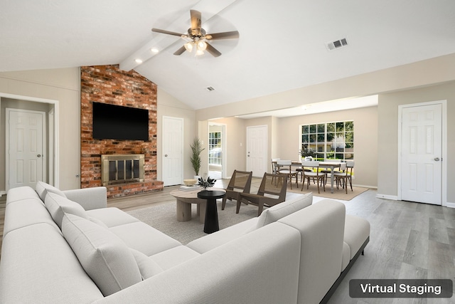 living room with vaulted ceiling with beams, light hardwood / wood-style floors, ceiling fan, and a brick fireplace