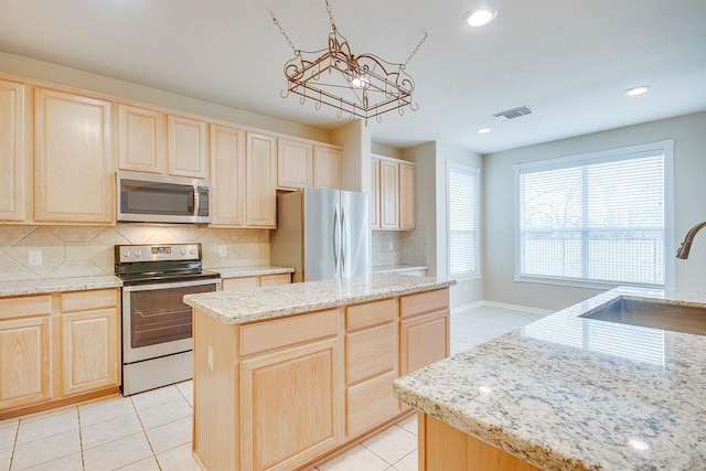 kitchen with light brown cabinets, a center island, decorative light fixtures, and appliances with stainless steel finishes