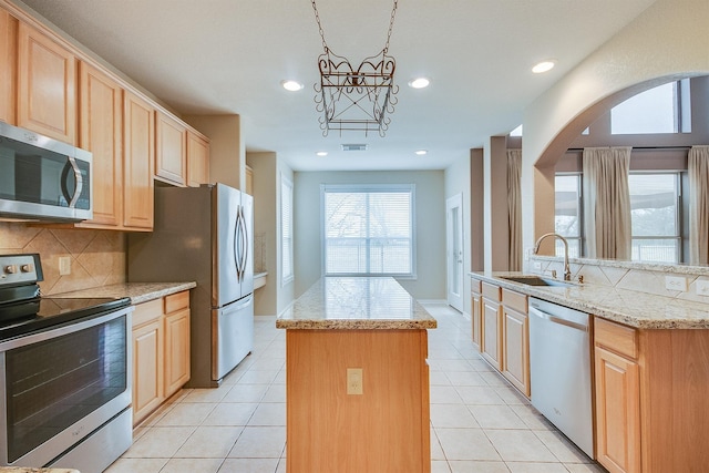 kitchen with light brown cabinetry, stainless steel appliances, sink, decorative light fixtures, and a center island