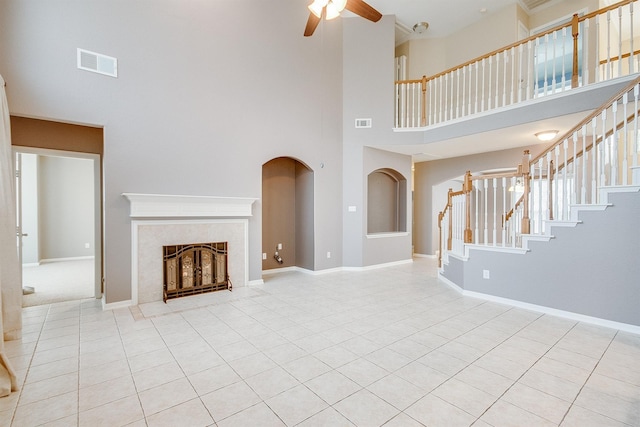 unfurnished living room featuring a tile fireplace, ceiling fan, a towering ceiling, and light tile patterned floors