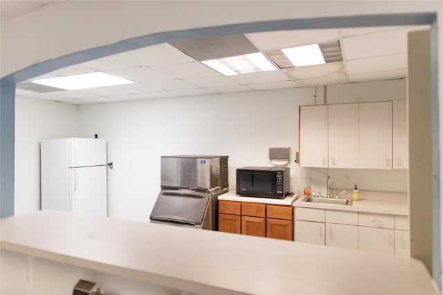 kitchen featuring refrigerator, a drop ceiling, sink, white refrigerator, and white cabinetry