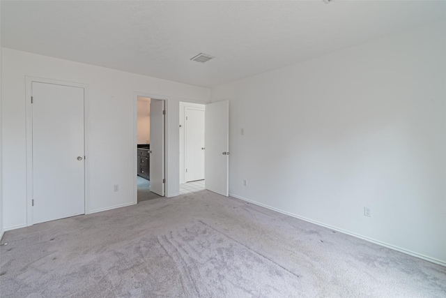 unfurnished bedroom with ensuite bath and light carpet