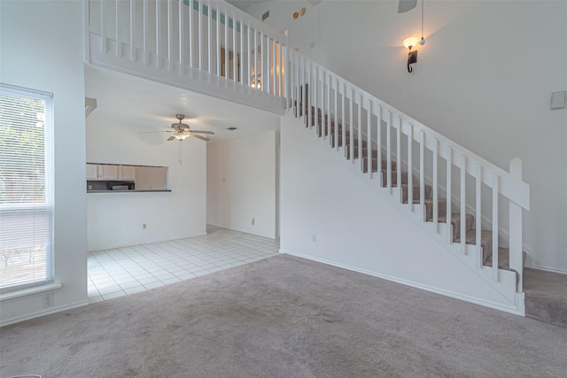 unfurnished living room with a high ceiling, light carpet, ceiling fan, and a wealth of natural light