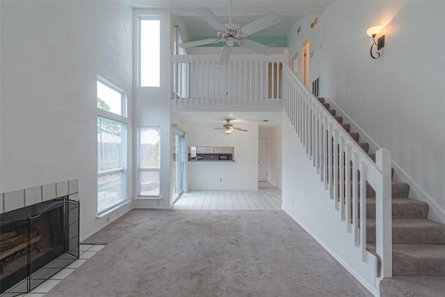 unfurnished living room featuring a fireplace, light carpet, a high ceiling, and ceiling fan