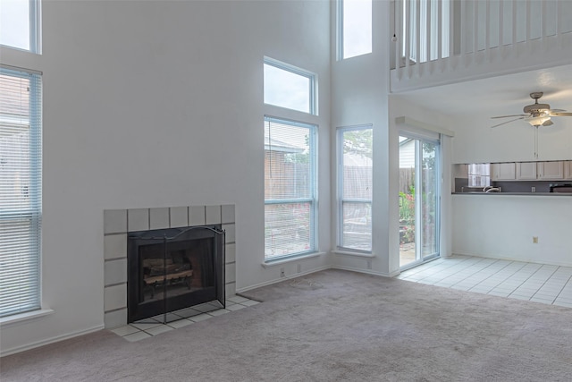 unfurnished living room featuring a tiled fireplace, a towering ceiling, light colored carpet, and plenty of natural light