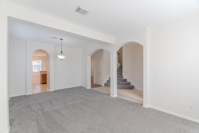 carpeted spare room with tile patterned floors, stairway, arched walkways, and visible vents