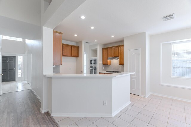 kitchen featuring kitchen peninsula, decorative backsplash, light tile patterned flooring, and appliances with stainless steel finishes