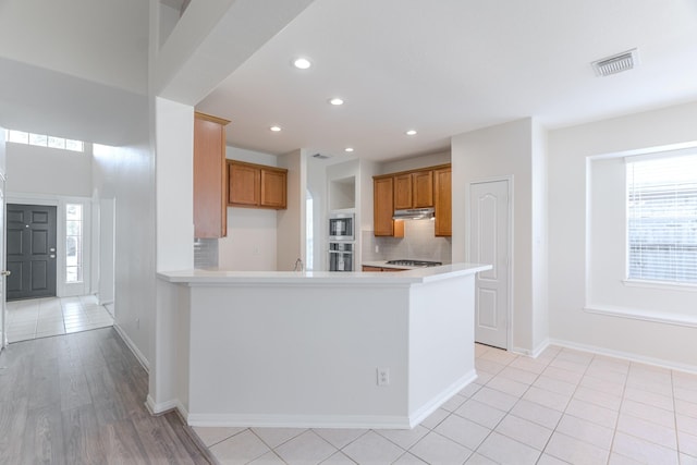 kitchen with visible vents, brown cabinets, under cabinet range hood, stainless steel appliances, and decorative backsplash