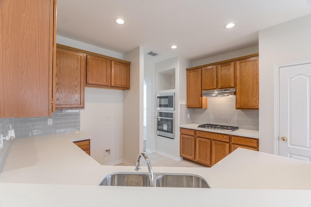 kitchen featuring visible vents, under cabinet range hood, appliances with stainless steel finishes, brown cabinetry, and a sink