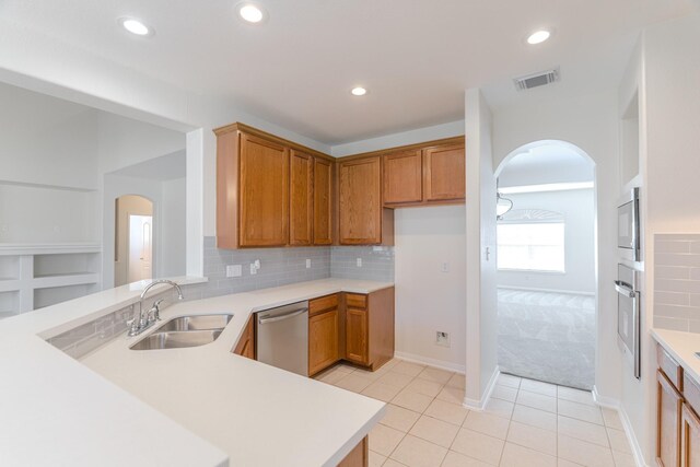 kitchen featuring sink, tasteful backsplash, kitchen peninsula, light colored carpet, and appliances with stainless steel finishes