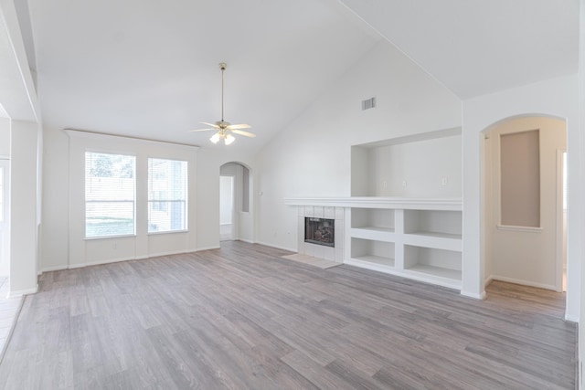 unfurnished living room featuring wood finished floors, high vaulted ceiling, arched walkways, ceiling fan, and a tiled fireplace