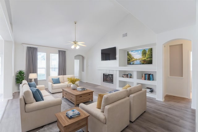 living room featuring light wood-type flooring, ceiling fan, high vaulted ceiling, built in features, and a fireplace