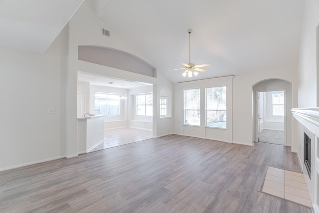 unfurnished living room with visible vents, a fireplace with flush hearth, high vaulted ceiling, light wood finished floors, and ceiling fan