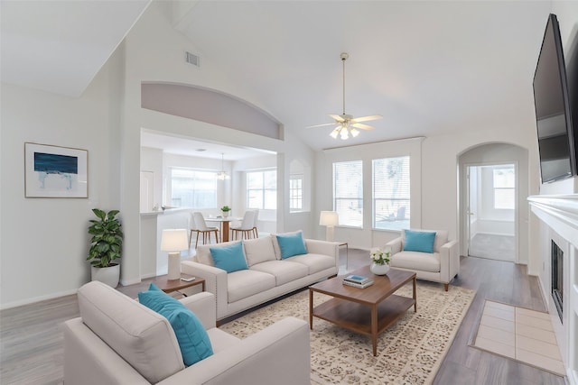 living room featuring baseboards, visible vents, high vaulted ceiling, a fireplace, and light wood-style floors