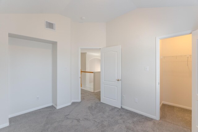 unfurnished bedroom with a spacious closet, a closet, light colored carpet, and lofted ceiling