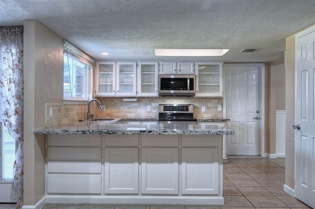 kitchen featuring light tile patterned floors, light stone counters, backsplash, white cabinets, and appliances with stainless steel finishes