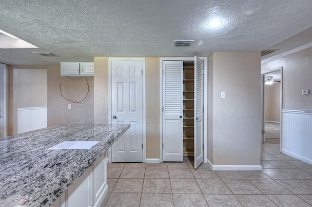 kitchen with ceiling fan, light tile patterned floors, a textured ceiling, light stone counters, and white cabinetry