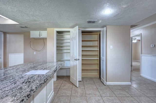 kitchen with white cabinets, ceiling fan, light tile patterned floors, a textured ceiling, and light stone counters