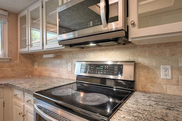 kitchen with light stone countertops, appliances with stainless steel finishes, tasteful backsplash, and white cabinetry