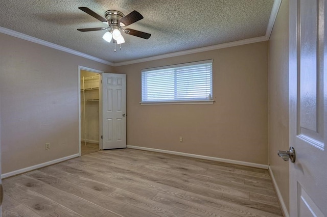 unfurnished bedroom featuring ceiling fan, crown molding, a spacious closet, and light wood-type flooring