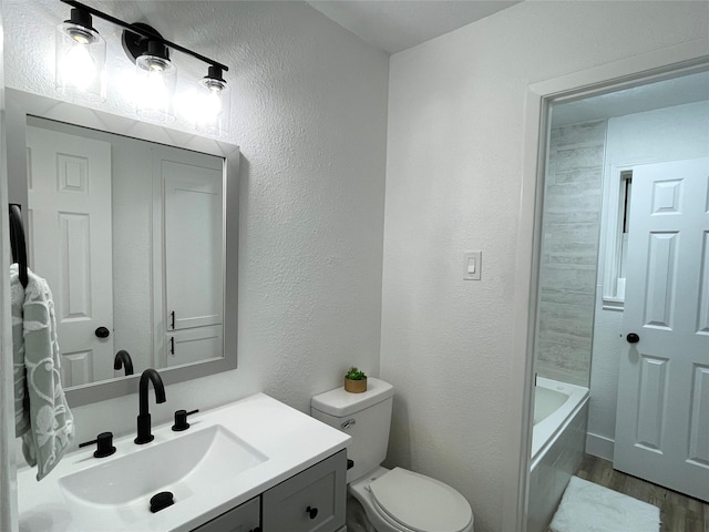 bathroom featuring hardwood / wood-style floors, vanity, toilet, and a washtub