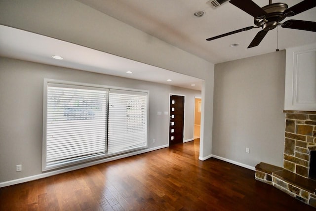 unfurnished living room with a stone fireplace, ceiling fan, and dark wood-type flooring